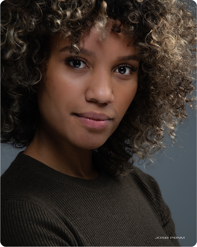 Woman with curly hair wearing a dark sweater against a gray background