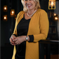 Woman wearing a yellow cardigan in a dimly lit room with hanging lights.